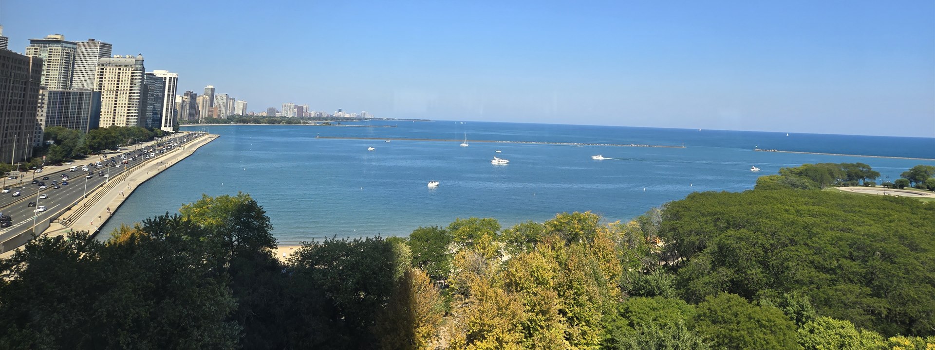 Lake Shore Drive curving north along the Lake Michigan shoreline, boats on the water and park trees in the foreground.